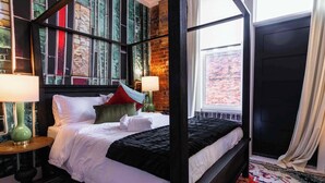 A four-poster bed with white linens, two bedside lamps, and a patterned rug.