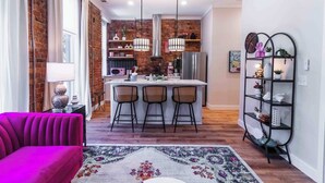 A modern kitchen with a central island, pendant lights, and a rustic brick wall.