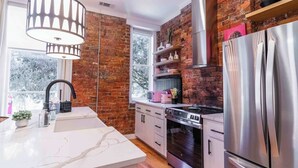 A modern kitchen with a marble countertop, stainless steel appliances, and a brick wall.