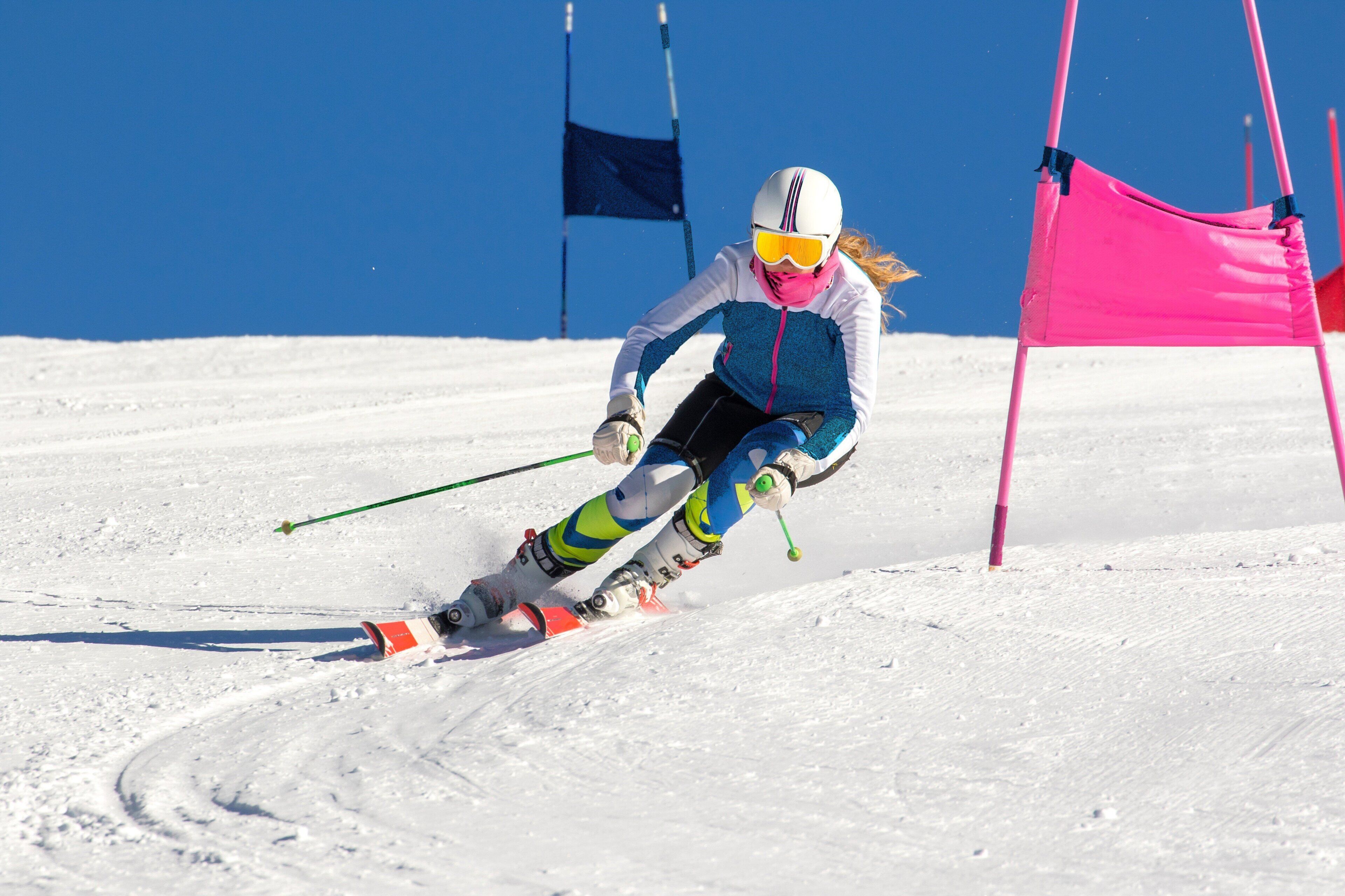 A skier in motion on a snowy slope with flags and a pink barrier in the background.