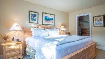 A bedroom with a wooden bed, two bedside tables with lamps, a nightstand with a plant, and two framed pictures on the wall.