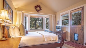 A bedroom with a large bed, a wooden dresser, a desk, a television, and a door with a window. - Cozy Ketchum Retreat - Pet Friendly! (Ketchum)