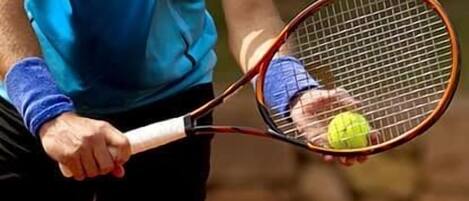 A person holding a tennis racket and a tennis ball on a clay court.