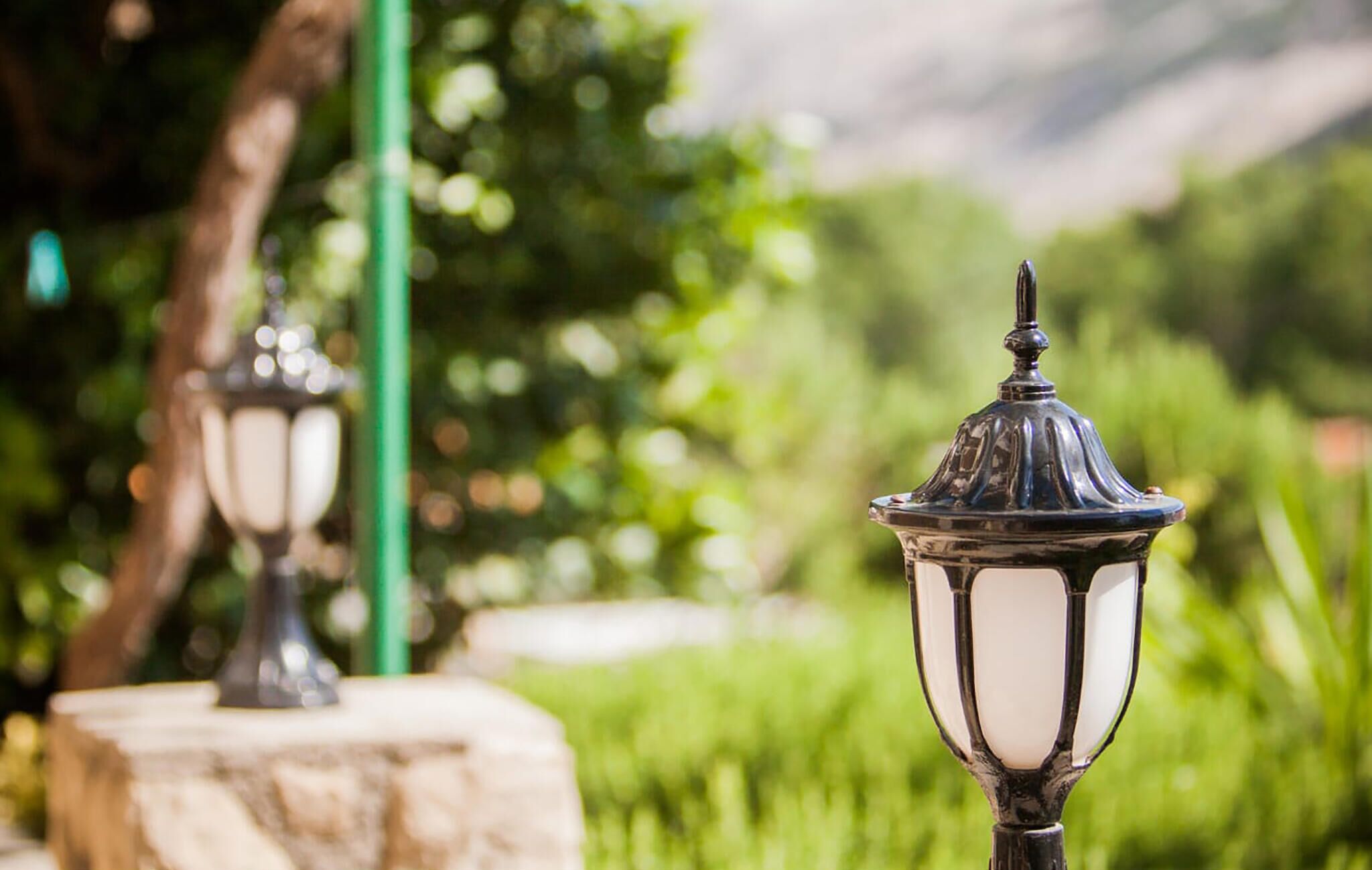 Lampadaires de style jardin, conçus pour l’extérieur, au design classique, se dressant sur un fond de verdure luxuriante, avec des arbres et une montagne en arrière-plan.
