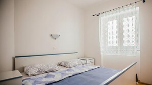 Quarto com uma cama de solteiro, mesa de cabeceira, luminária na parede e janela com cortina estampada.