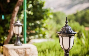 Outdoor garden-style lighting fixtures with a classic design, set against a lush green background with a blurred mountain view. - 1 bedroom beautiful apartment in Lopar (Lopar)