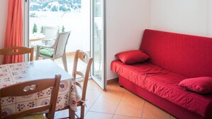 Quarto com uma mesa de jantar, cadeiras, um sofá vermelho e vista para montanhas através de uma porta de vidro.