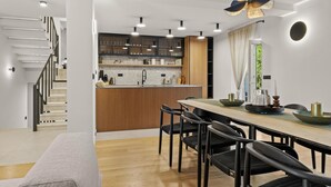 A modern kitchen with a central island, a dining area with a wooden table and black chairs, and a staircase with a white railing. - Luxurious home in Opric with sauna (Opric)