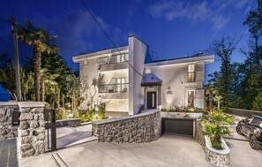 Une villa moderne à deux étages, dotée d’une façade en pierre, d’un garage et d’un jardin aménagé.