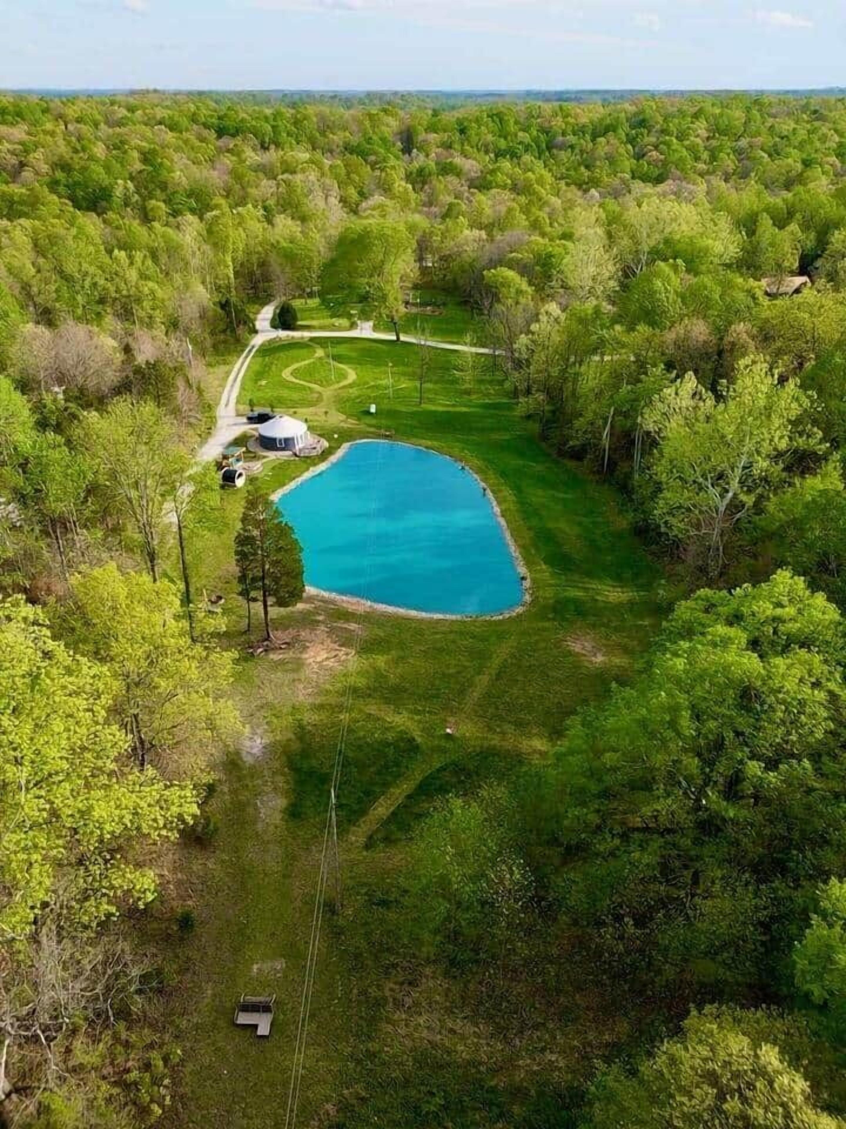 An aerial view of a property with a large blue pool surrounded by lush greenery and a winding path.