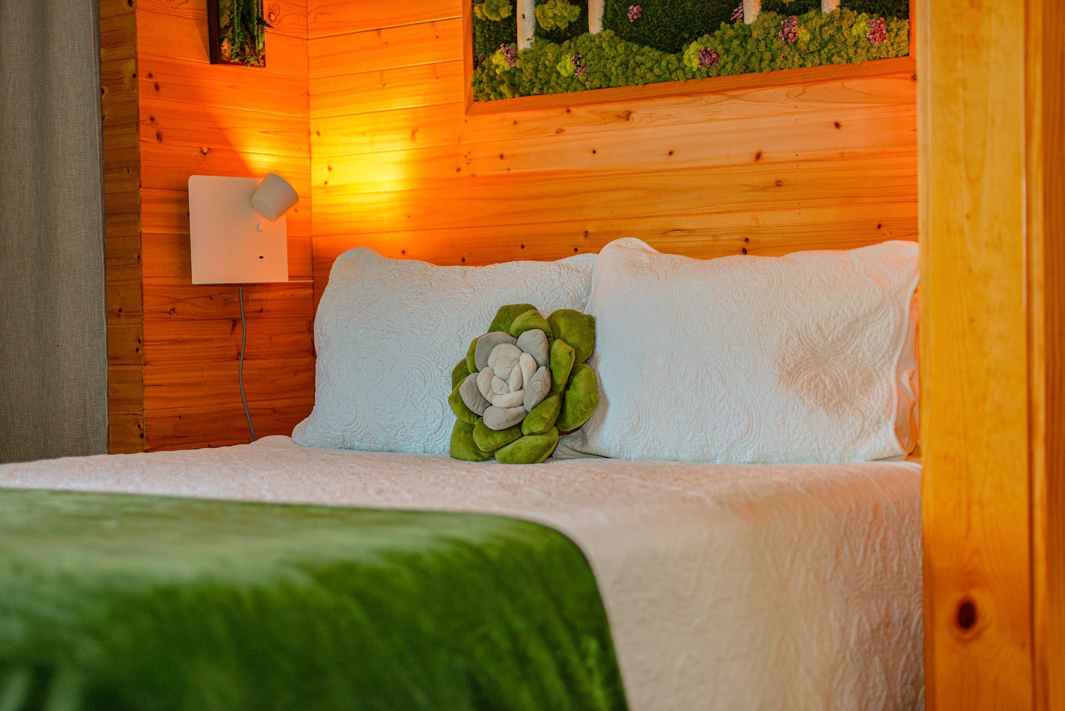 A wooden-paneled room with a bed, a wall-mounted light, and a decorative plant.