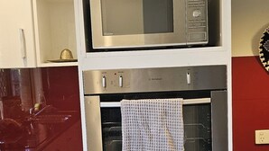 A kitchen with a microwave and oven, white cabinetry, and a red backsplash.