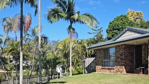 A residential property with a stone house, a grassy yard, and palm trees.