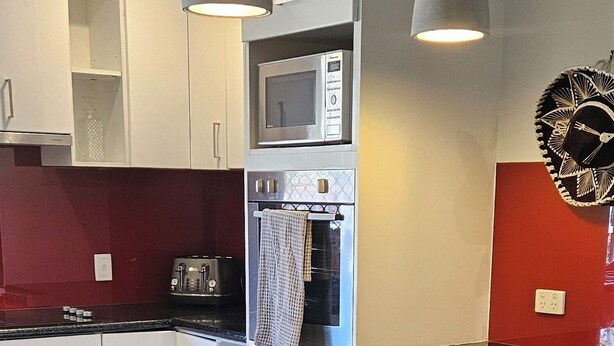 A modern kitchen with a central island, two pendant lights, a microwave, and a red accent wall.