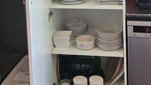 A kitchen pantry with shelves of dishes, glasses, and a recycling bin.