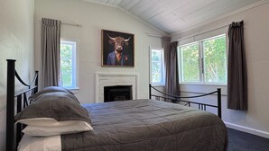 Une chambre à coucher avec un grand lit, une cheminée et deux fenêtres avec des rideaux.