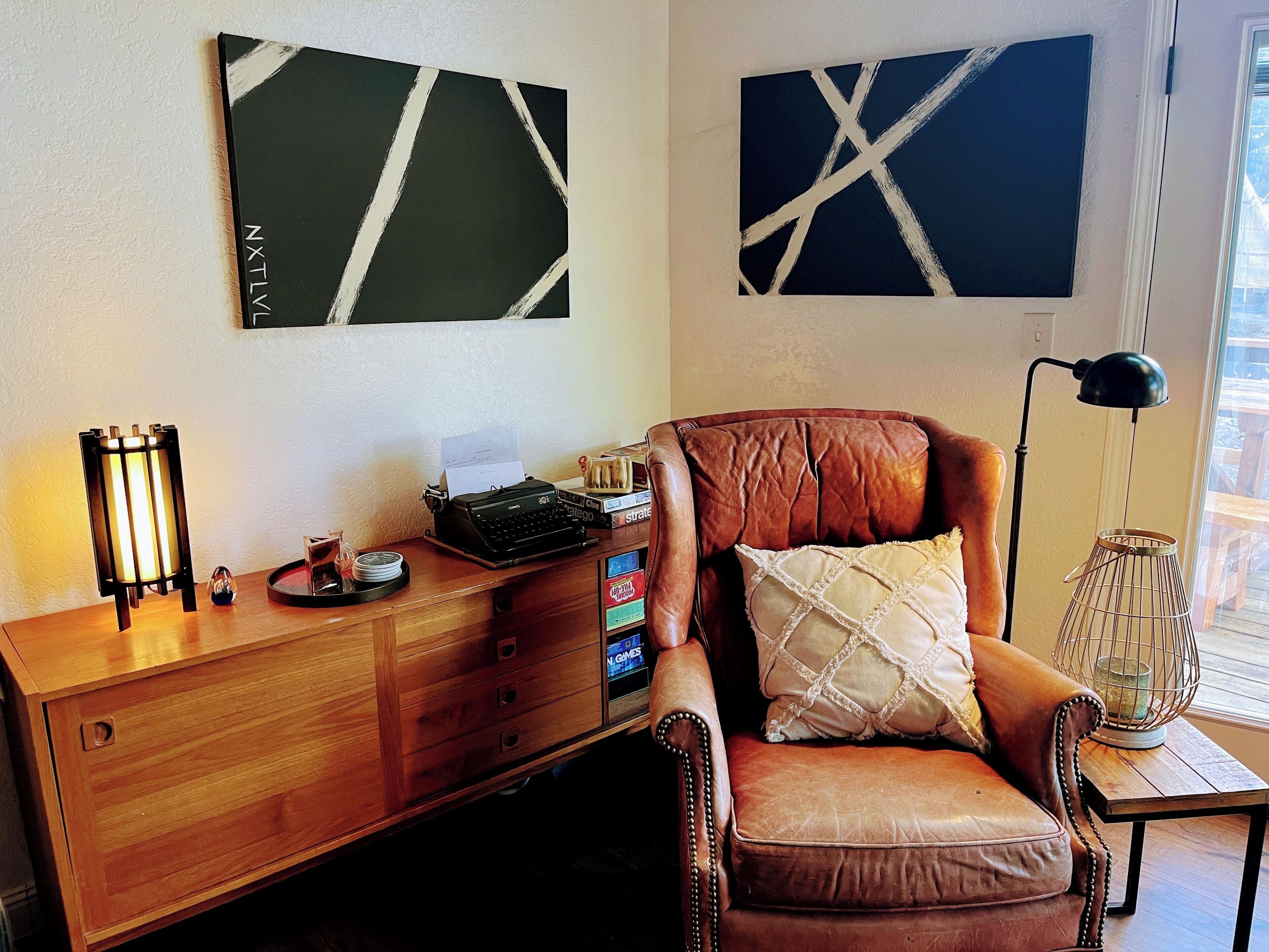 A room with a wooden desk, a leather chair, a typewriter, and abstract wall art.