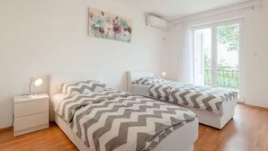 Une chambre avec deux lits, une table de chevet, un climatiseur fixé au mur et une fenêtre donnant sur un paysage verdoyant.