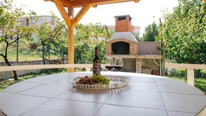 Une terrasse extérieure avec une table ronde, une bouteille de vin et un bol de raisins.