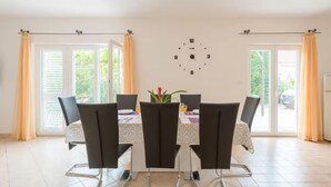 Un coin repas avec une table dressée pour quatre personnes, une horloge murale et de grandes fenêtres avec des rideaux.