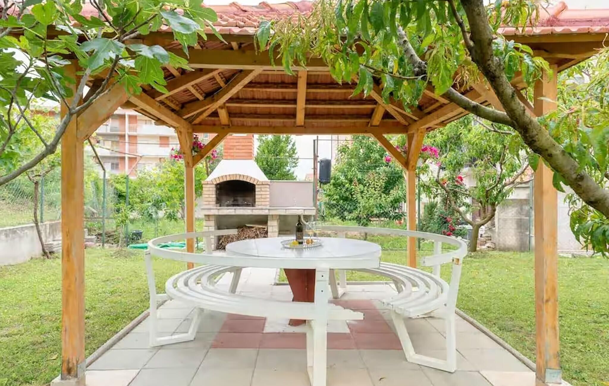 A covered outdoor dining area with a circular table and a brick oven in the background.
