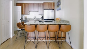 A modern kitchen with wooden cabinets, a stainless steel refrigerator, a granite countertop, and four bar stools. - 3-bedroom townhome in beautiful Key West with AC and charm (Key West)