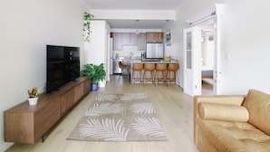 A modern living room with a flat-screen TV, a brown leather sofa, a patterned rug, and a wooden entertainment unit. - 3-bedroom townhome in beautiful Key West with AC and charm (Key West)
