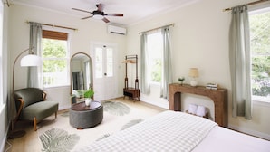 A bedroom with a bed, a chair, a mirror, a fireplace, and a ceiling fan. - 3-bedroom townhome in beautiful Key West with AC and charm (Key West)