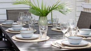 A dining table set with plates, bowls, glasses, and a vase with green foliage. - 3-bedroom townhome in beautiful Key West with AC and charm (Key West)