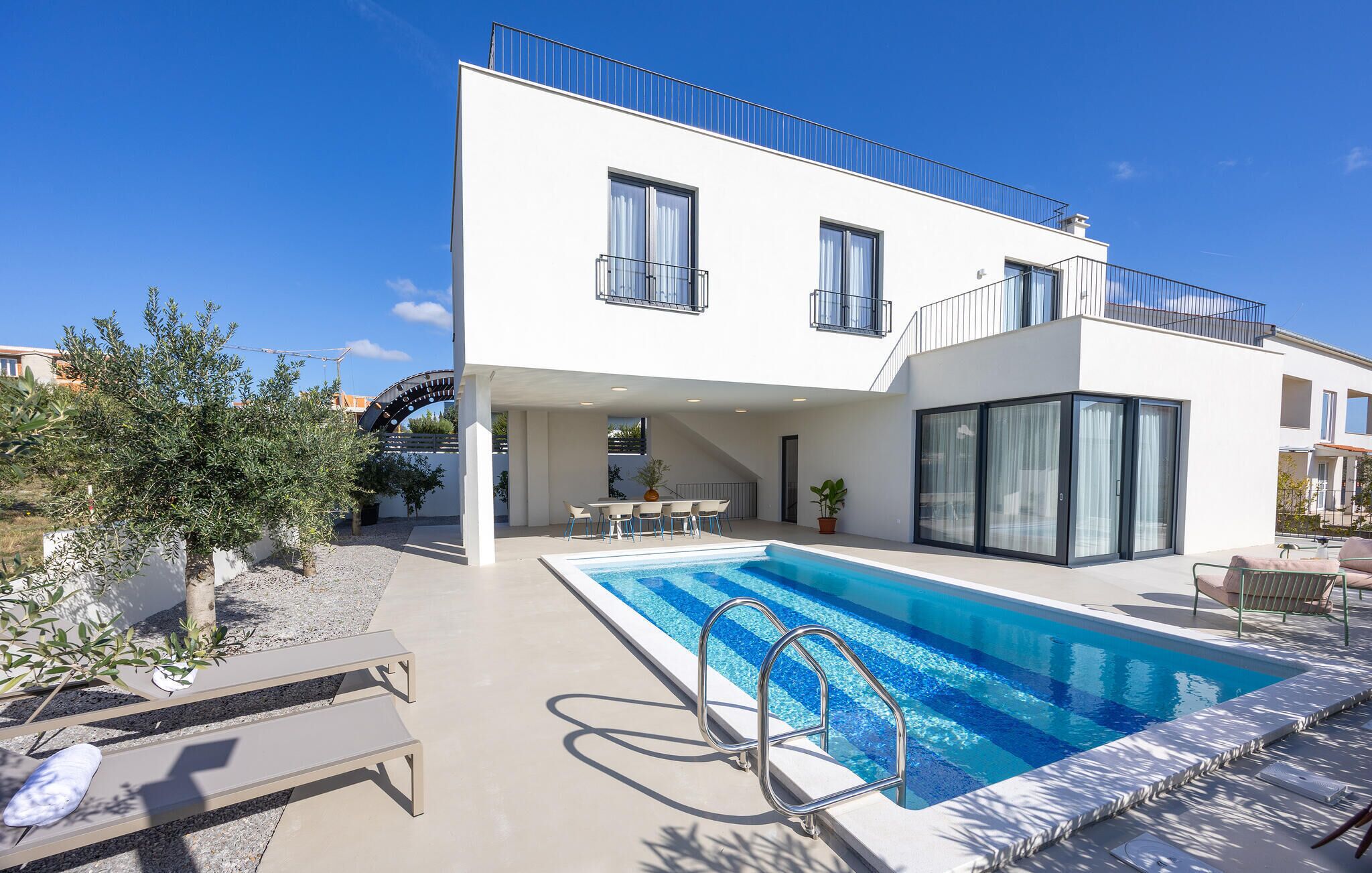 A modern two-story house with a swimming pool, outdoor seating, and a covered patio area.