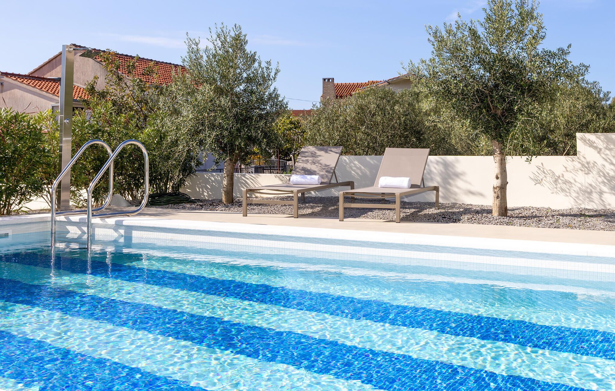 Une piscine à l’eau d’un bleu cristallin, entourée de chaises longues et d’arbres.