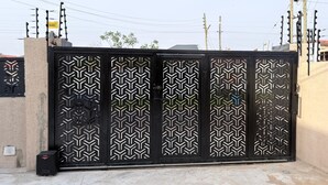 Una reja de metal negro con diseños geométricos, un cesto de basura pequeño y postes de servicios al fondo.