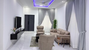 Una sala de estar moderna con un televisor de pantalla plana, un sofá color beige, una silla y una mesa de centro.