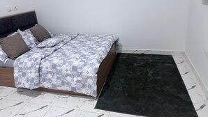 Un dormitorio con cama, alfombra negra y suelo de baldosas blancas.