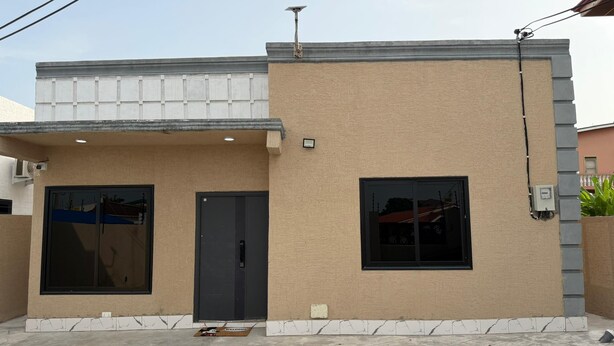 Un edificio de dos pisos con fachada color beige, una puerta oscura y una ventana.