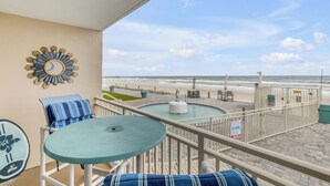 Un balcone con vista sulla spiaggia, un tavolo rotondo, una sedia con cuscino a righe e un elemento decorativo a parete.