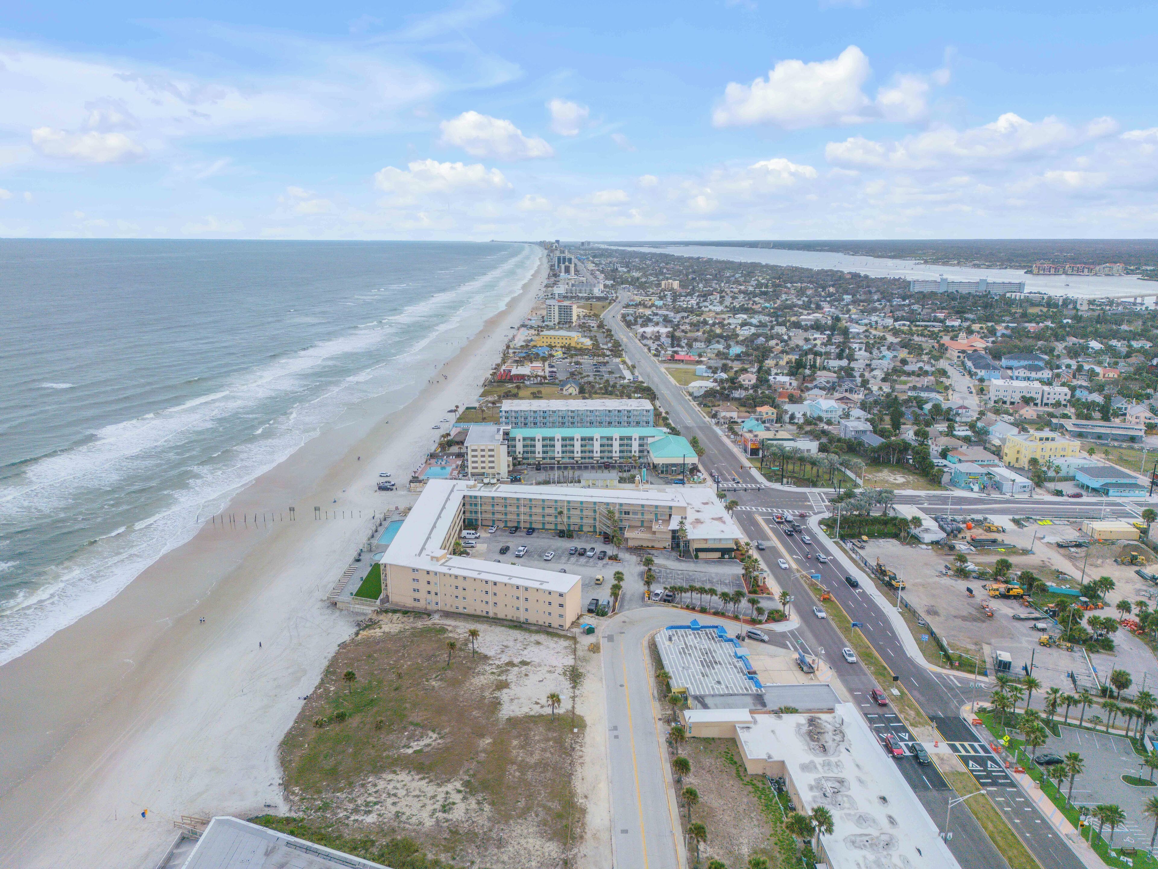Luftaufnahme einer Küstenstadt mit Strandhotel, Straßen und umliegenden Wohngebieten.