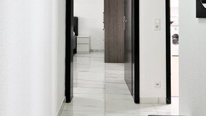 Um corredor moderno com piso de mármore, porta de madeira e espelho com moldura preta.