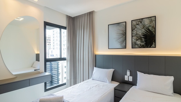 A modern hotel room with a bed, bedside tables, a large mirror, and artwork on the wall. - Apto c\/ Varanda Gourmet próximo ao Mar OZN1004 (Itapema)