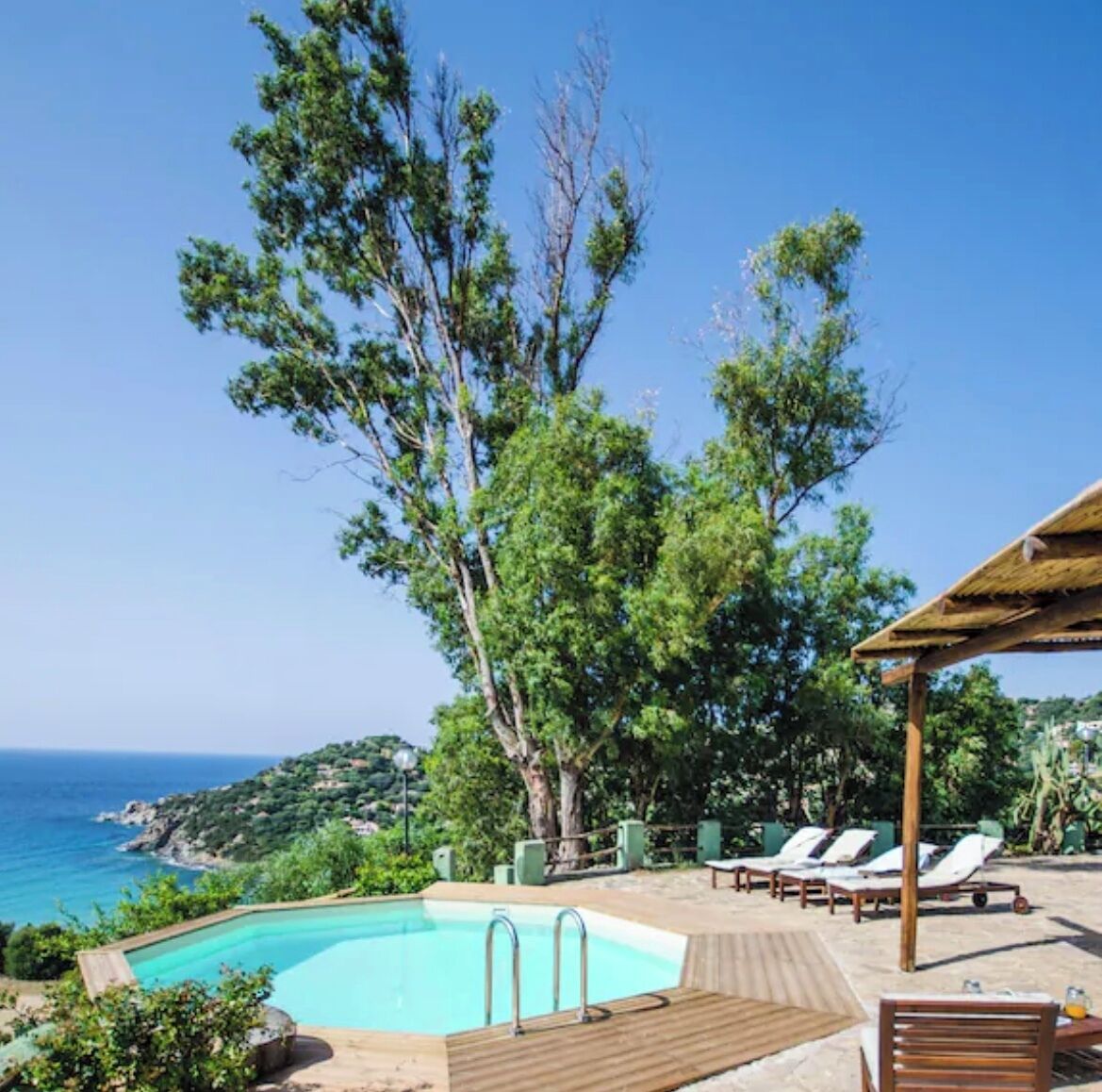 A poolside area with lounge chairs, a wooden deck, and a view of the sea.