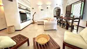 A modern living room with a sofa, wooden coffee table, and a dining area with chairs and a table. - Seaview villa, design, comfort and privacy, pool, sandy, white beach 5 min walk (Sardegna)