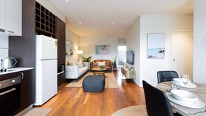 Een modern appartement met keuken, eethoek en woonkamer. Het heeft houten vloeren, een bank, salontafel en televisie.