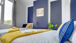 Habitación de hotel con dos camas, un ventanal grande, un cuadro en la pared y una planta.