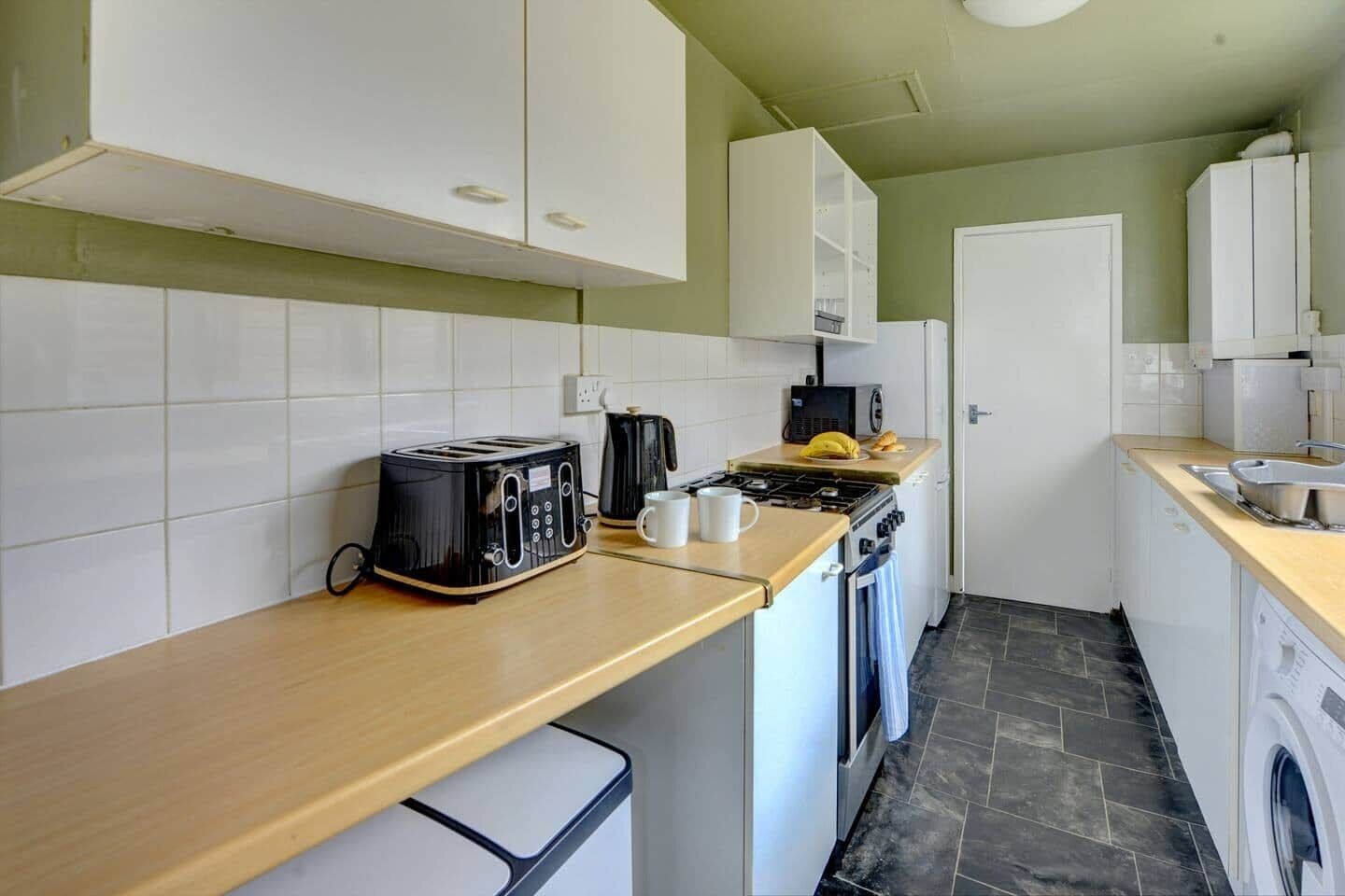 Een kleine keuken met witte kastjes, een broodrooster, een koffiezetapparaat en een fornuis.