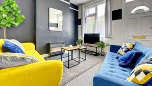 Una sala de estar con un sofá amarillo, un sofá azul, un televisor, una mesita y una planta en maceta.