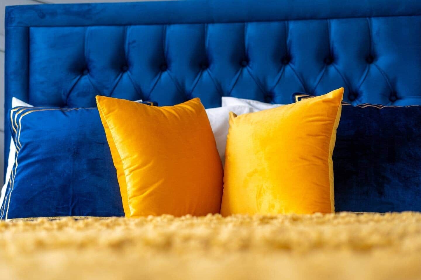Ein Bett mit einem blau gepolsterten Kopfteil und zwei gelben Kissen.