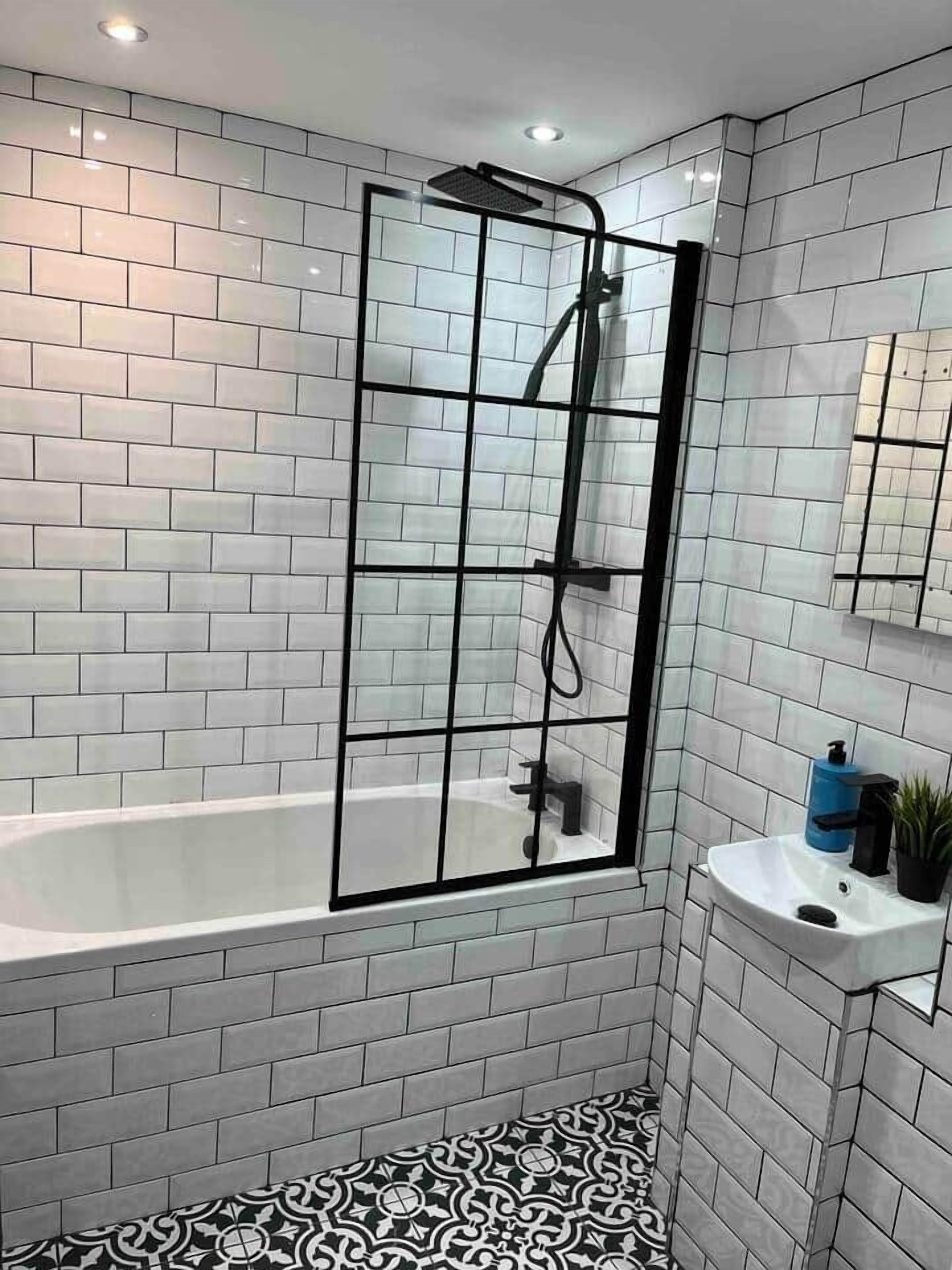 A modern bathroom with white subway tiles, a glass shower enclosure, a white bathtub, and a black and white patterned floor.