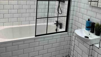 A modern bathroom with white subway tiles, a glass shower enclosure, a white bathtub, and a black and white patterned floor.