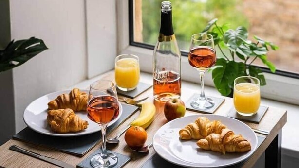 Colazione su un tavolo vicino a una finestra, con croissant, succo di frutta e una bottiglia di vino.
