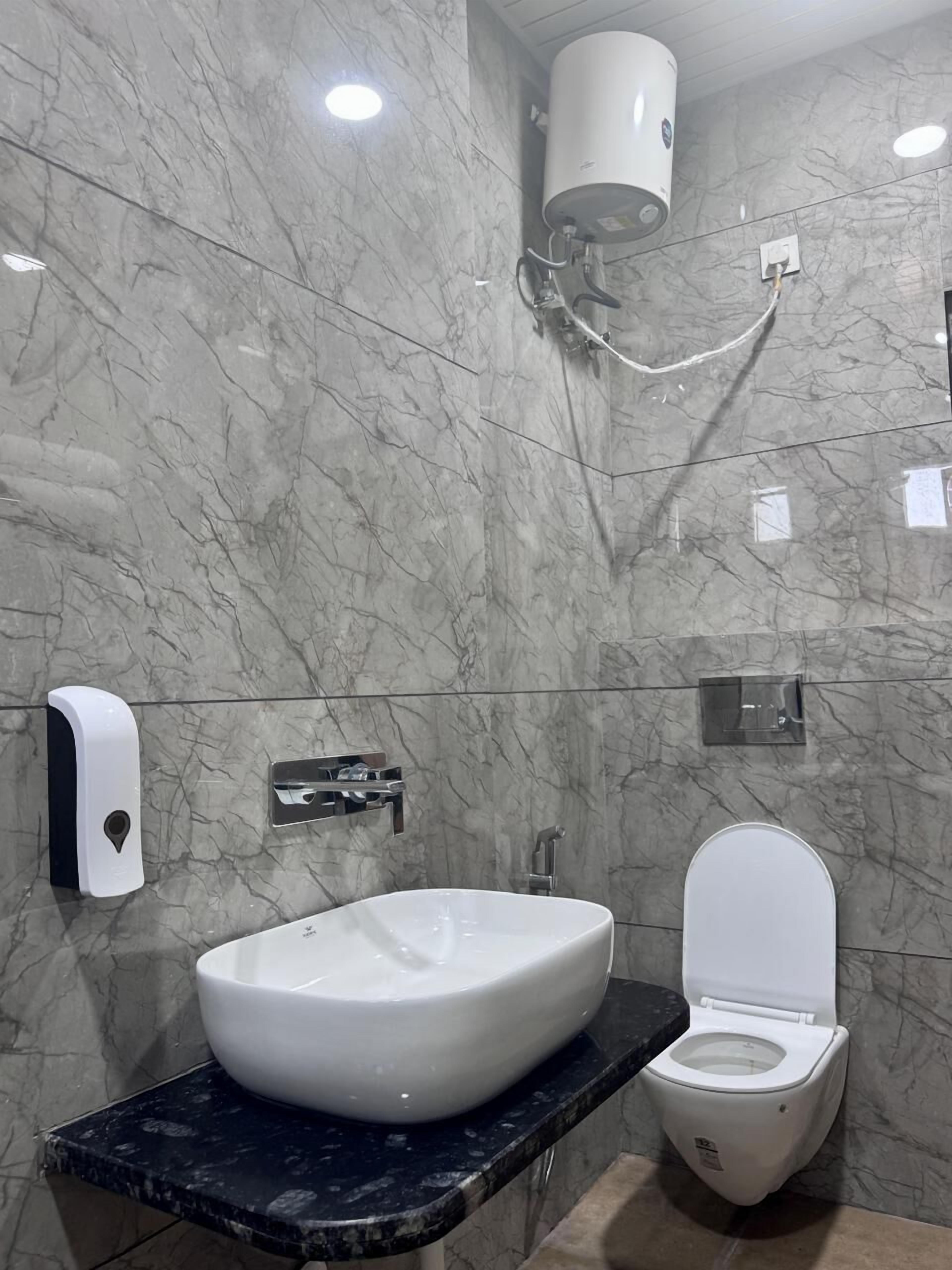 A bathroom with a marble wall, a white sink, a toilet, a hand dryer, and a towel rack.
